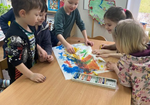 Dzieci pochylone nad kartką malują smoki